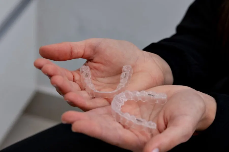 A pair of clear orthodontic aligners held in an open hand