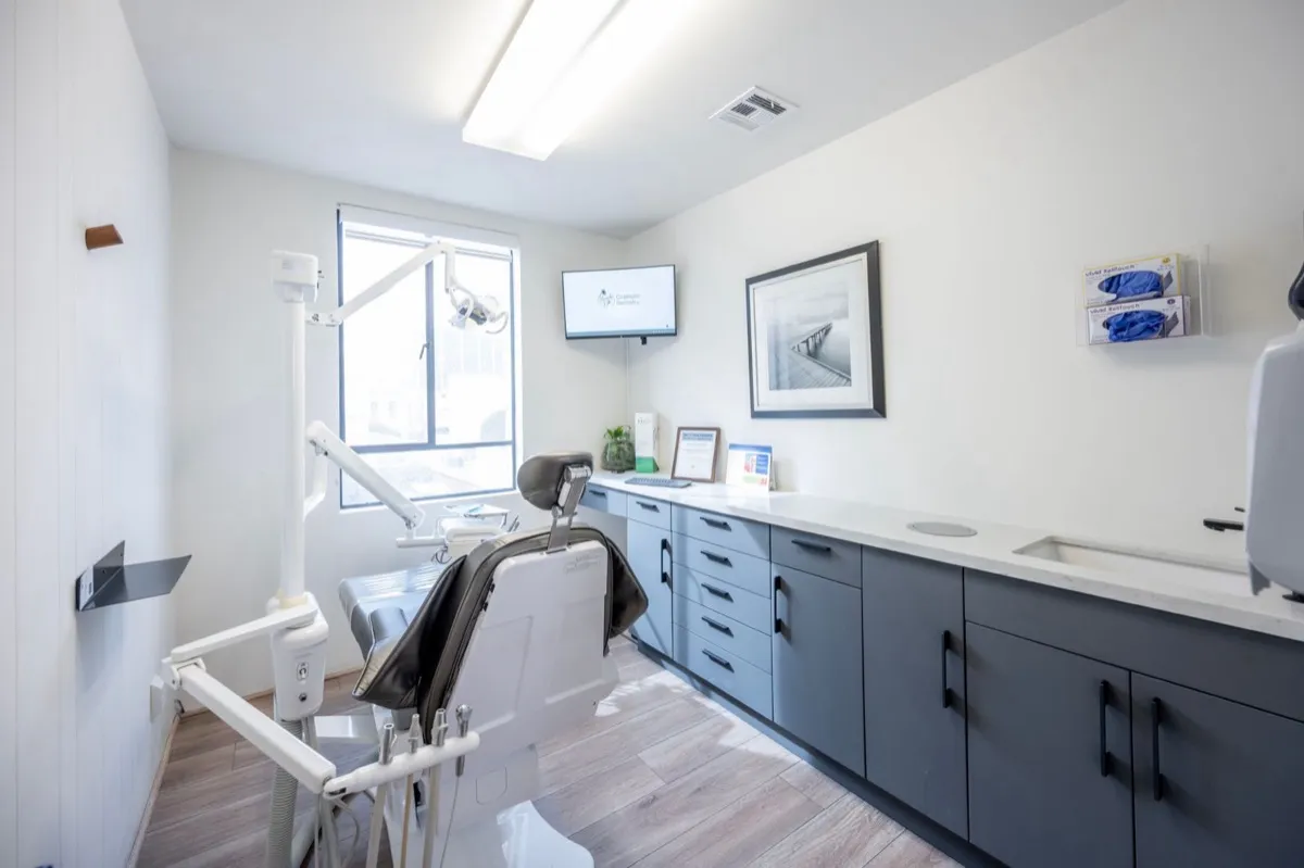 A modern dental treatment room with a chair, overhead light and cabinetry